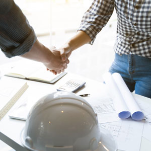 Two professionals shaking hands at a table, surrounded by construction plans - Jones Law Firm